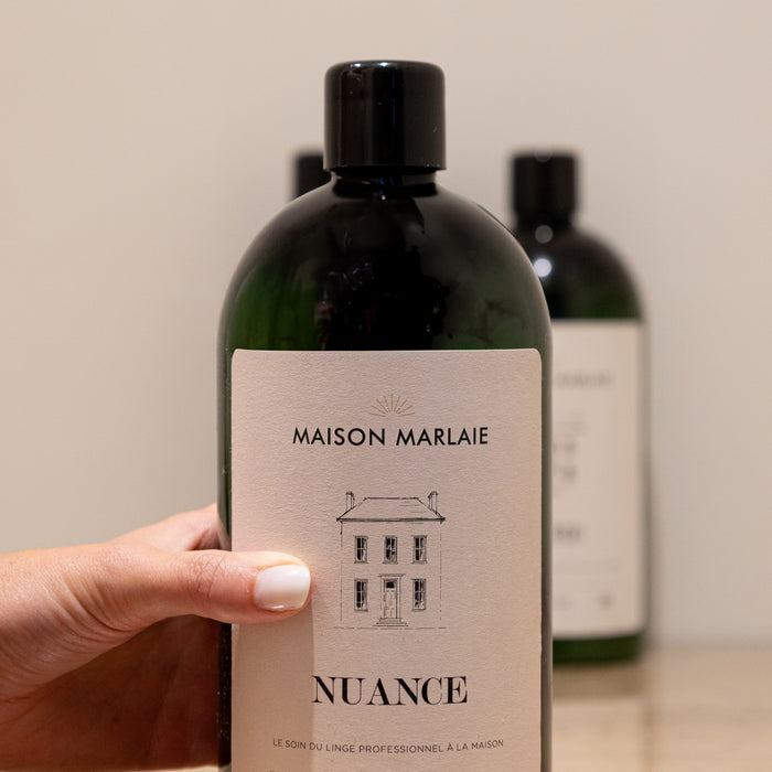 Hand picking a NUANCE bottle in front of the Maison Marlaie range