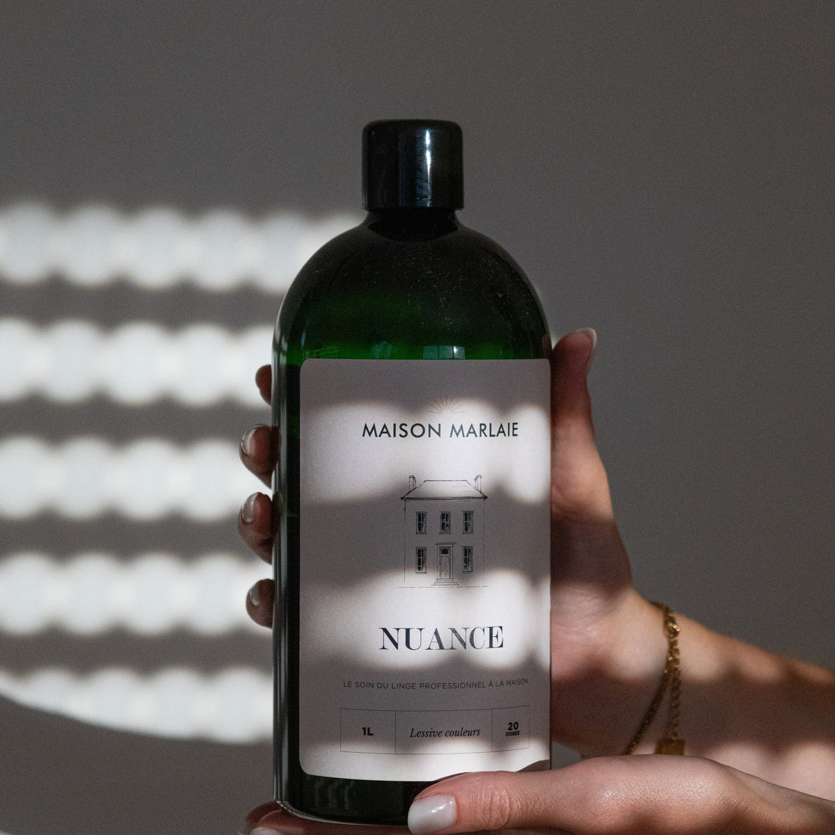 Hand holding a Maison Marlaie NUANCE bottle in the light of a blind