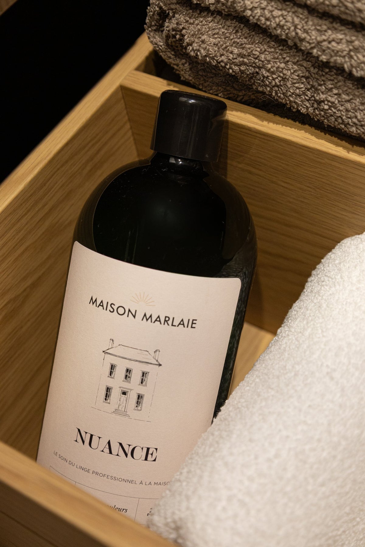 Le flacon Nuance dans un meuble en bois, pres d'une serviette en bouclette